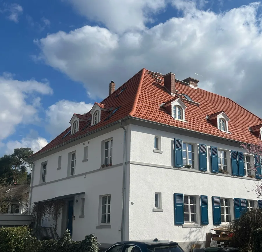 Denkmalgeschütztes Offiziershaus von 1920: weiß verputzter Bau mit rotem Walmdach, erhaltenen Gauben und blaugrünen Fensterläden, dazwischen neue Dachflächenfenster.