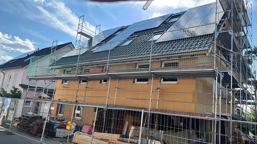 Der Holzrohbau während der Fertigstellung: eingerüstete Fassade mit Holzfaserplatten, auf dem Dach die bereits verlegte Photovoltaikanlage.